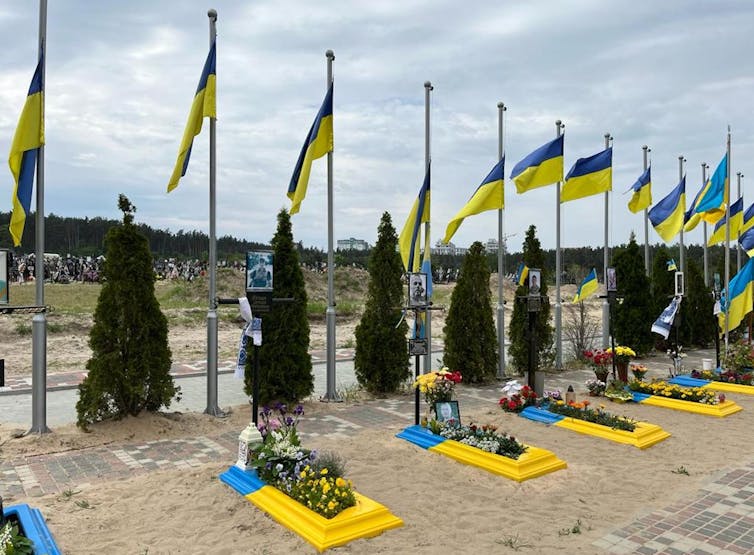 Tombes fleures peintes aux couleurs du drapeau ukrainien, chacune étant surmontée d’un grand drapeau ukrainien
