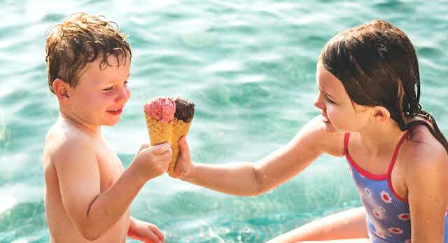 dos niños comiendo helado en una piscina, hace calor