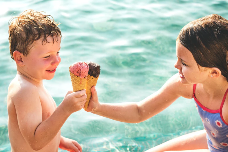 dos niños comiendo helado en una piscina, hace calor
