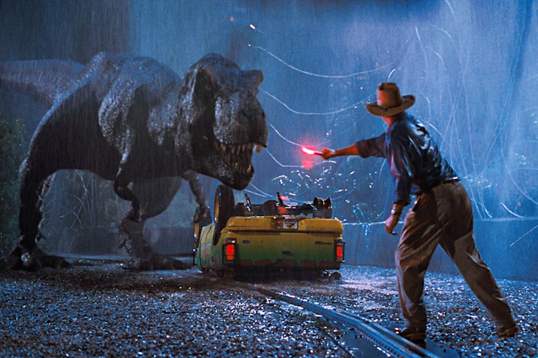 A T.rex stands over an upturned yellow car while a man in te foreground waves a bright red flare at it.
