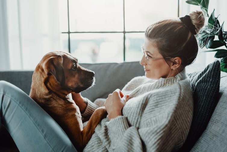 A woman sits with her dog on the couch.