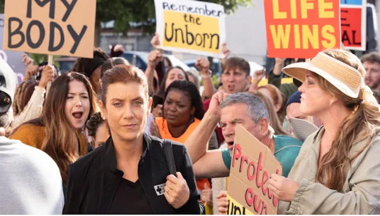 Woman wades through a crowd of screaming protesters.