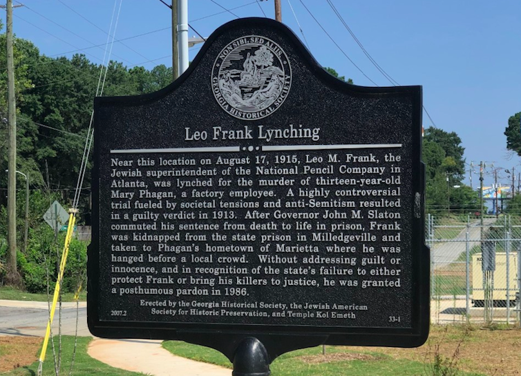 A rectangular historic marker on a pole outside, with the heading 'Leo Frank lynching,' describing the circumstances of Frank's death.