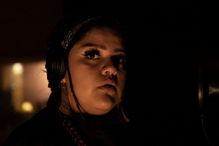 A young woman's face, with a serious expression, lit up against a dark room.