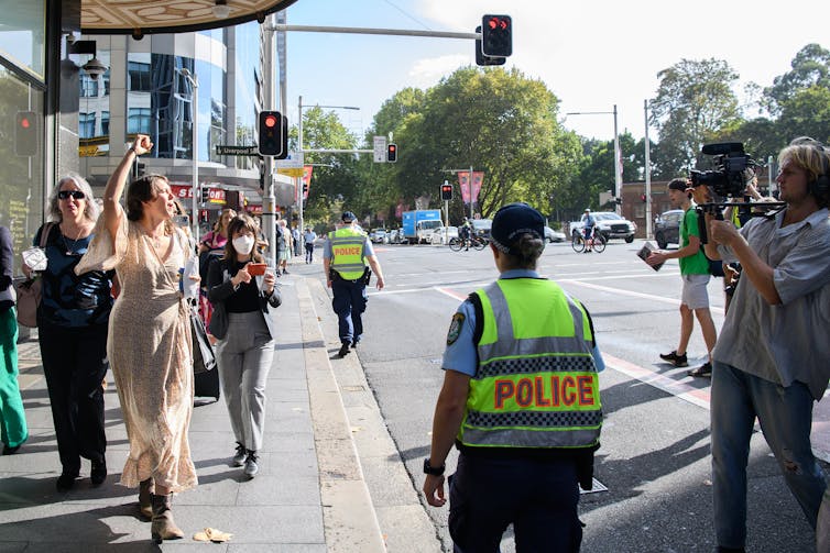 picture of a woman activist chanting slogans on the street while police overlooks