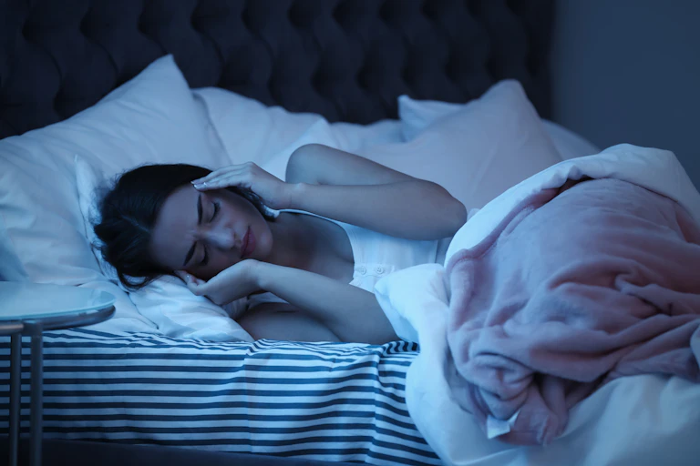A woman lying in bed at night puts her hands to her temples.