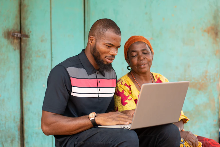A young Black man sat with his grandmother, both of them looking at a laptop.