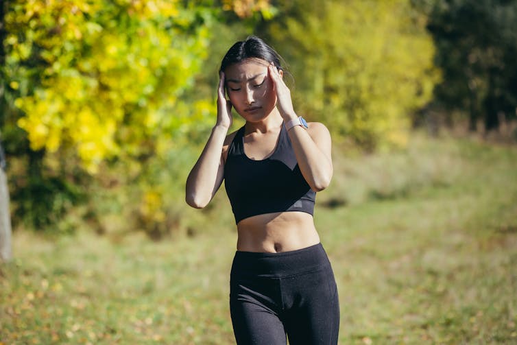 A young female runner holds her head in pain.