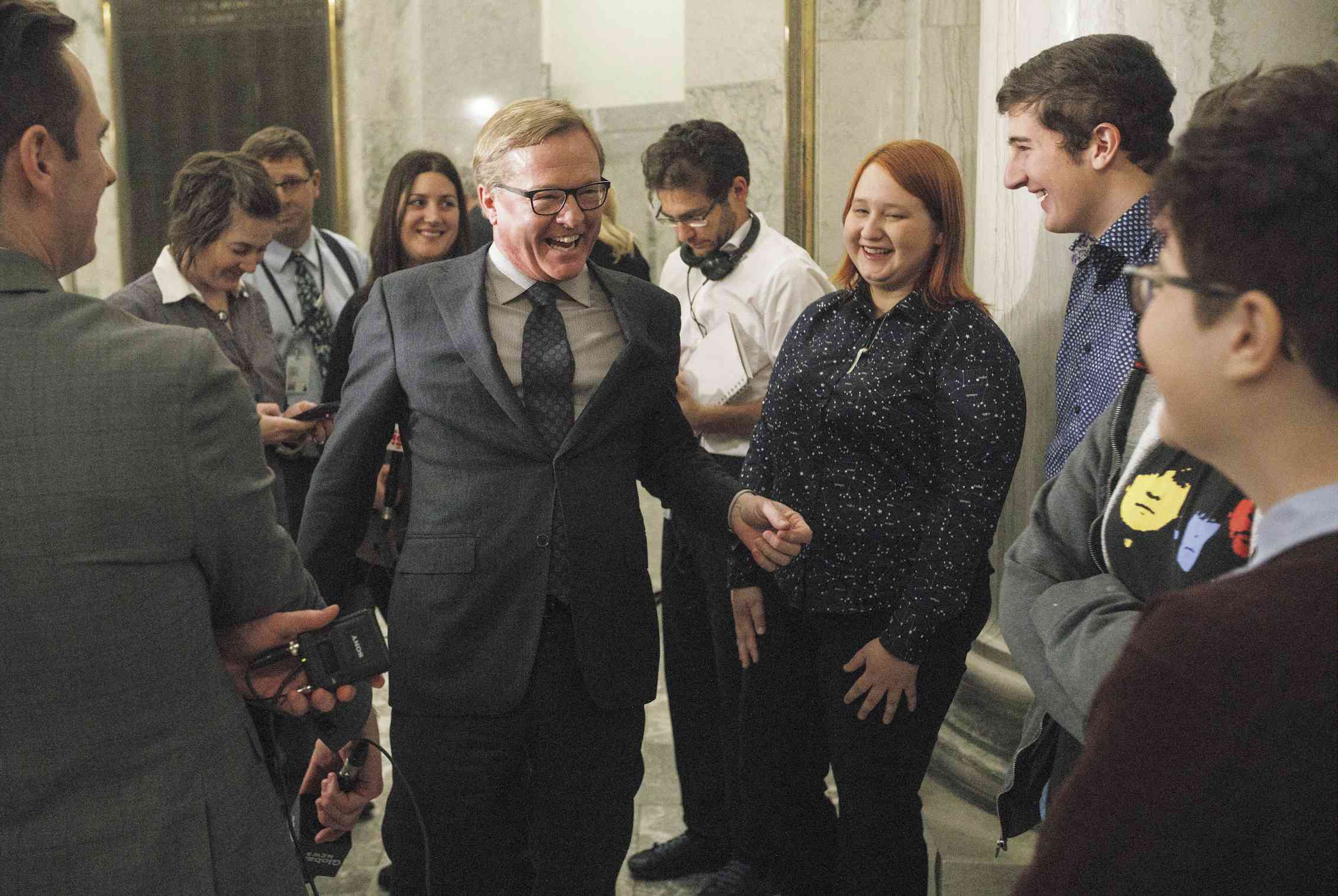 A man in a suit walks among smiling young people.