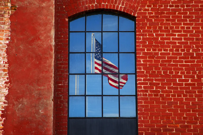 A brick wall with windows shows the reflection of a fractured American flag.