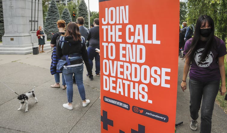Protesters hold up an orange sign with white text that reads Join the Call to End Overdose Deaths.