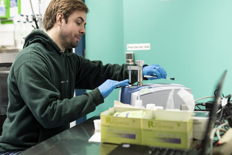A bearded man wearing blue rubber gloves tests drug samples with an infra-red machine.