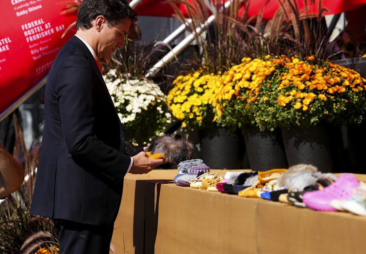 A dark haired man places a pair of small shoes on a table with other shoes.