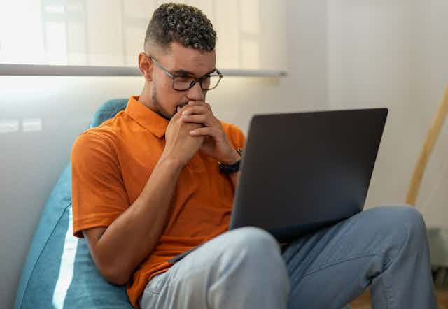 man folds hands over mouth looking at laptop