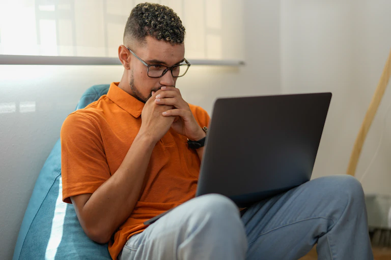 man folds hands over mouth looking at laptop