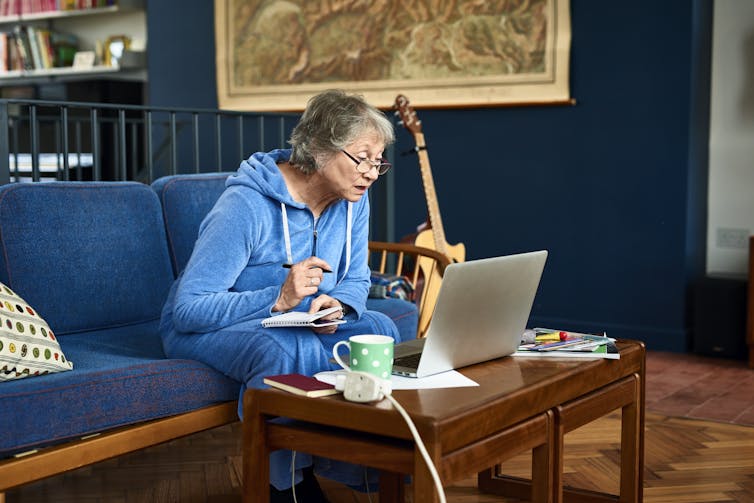 woman looks confused taking notes on paper looking at laptop