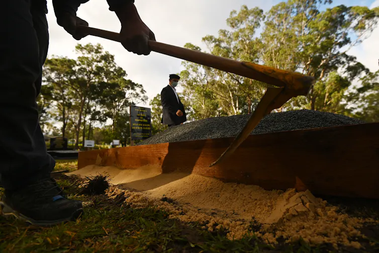 A cemetery work starts filling a grave with dirt