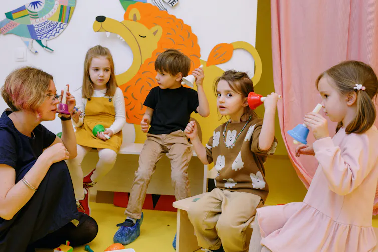 A woman sits with young children, experimenting with bells.