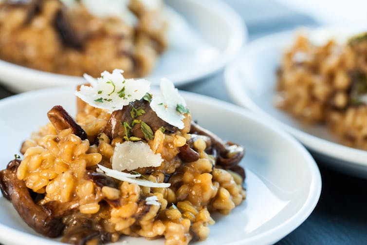 Gros plan sur un risotto aux champignons doré, surmonté de copeaux de parmesan