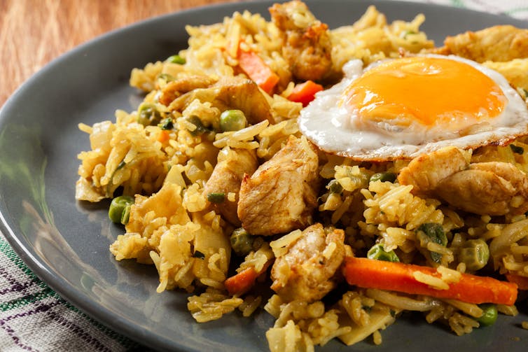 نمای نزدیک از یک ظرف برنج سرخ شده با مرغ، سبزیجات و یک تخم مرغ آفتابی در بالا