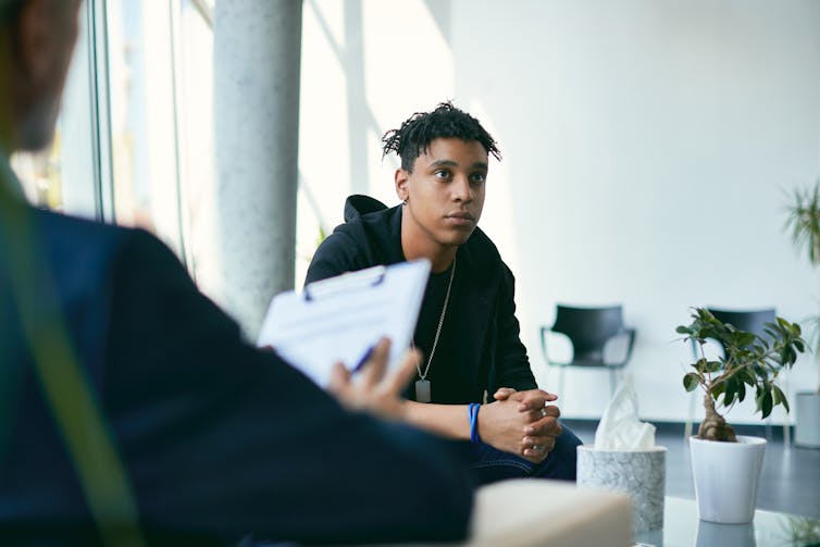 Teenage boy having counselling with mental health professional during therapy session.