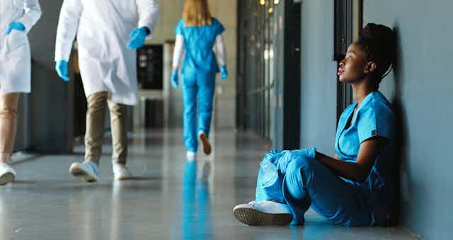 A female healthcare worker sits on the floor in a hospital corridor.