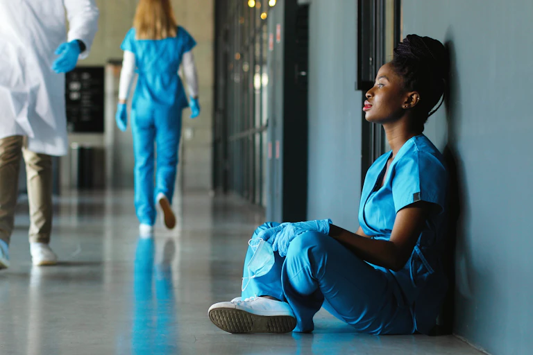 A female healthcare worker sits on the floor in a hospital corridor.