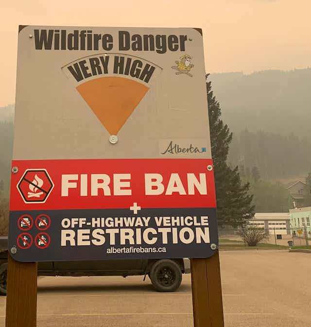 A wildfire danger sign seen with the words "fire ban" against a hazy sky.