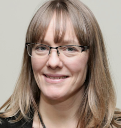 A headshot of a bespectacled blonde woman, Angela Rodel, smiling at the camera.