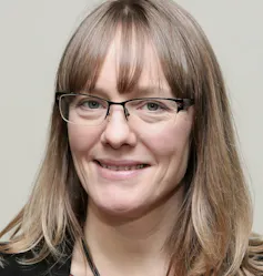 A headshot of a bespectacled blonde woman, Angela Rodel, smiling at the camera.