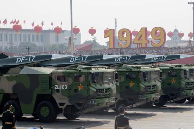 Large military vehicles carry missiles with pointed tips in a military parade 