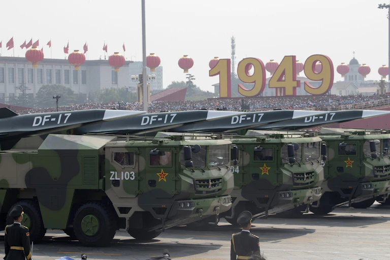 Large military vehicles carry missiles with pointed tips in a military parade