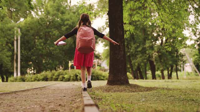 Una niña camina por un parque con una mochila en la espalda.