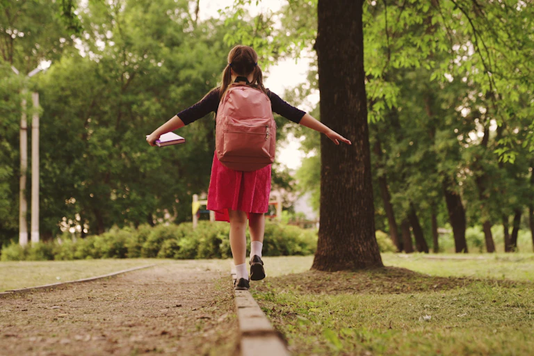 Una niña camina por un parque con una mochila en la espalda.