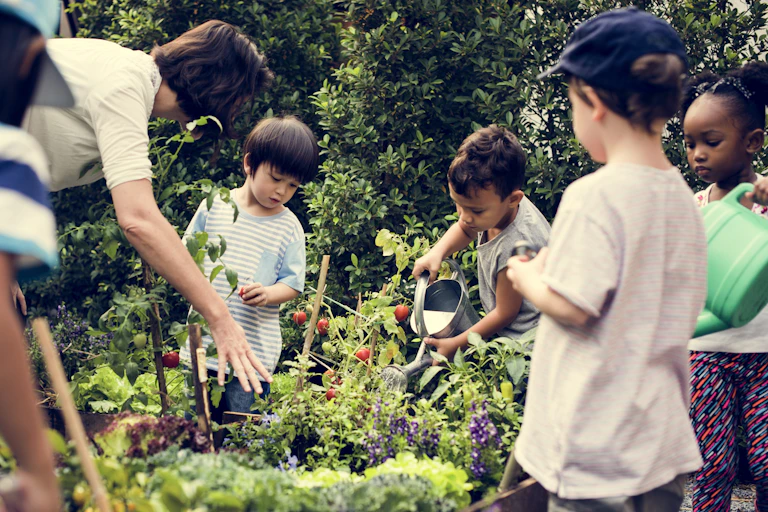 Children seen standing around a garden holding cans and touching plants.