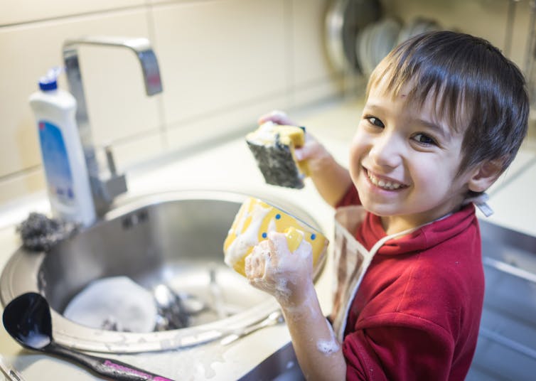 A boy seen with a sponge washing dishes.