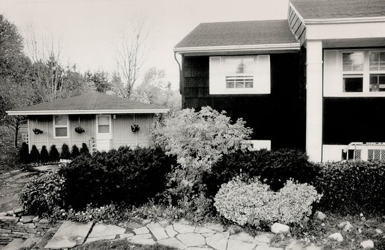 Black and white photo of a small home built behind a larger home.