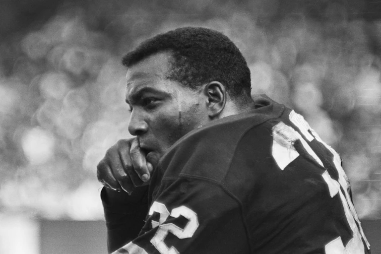 A black man wearing a football uniform is sitting on a bench.