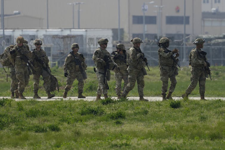 A row of soldiers in battle fatigues walk along a grassy path.