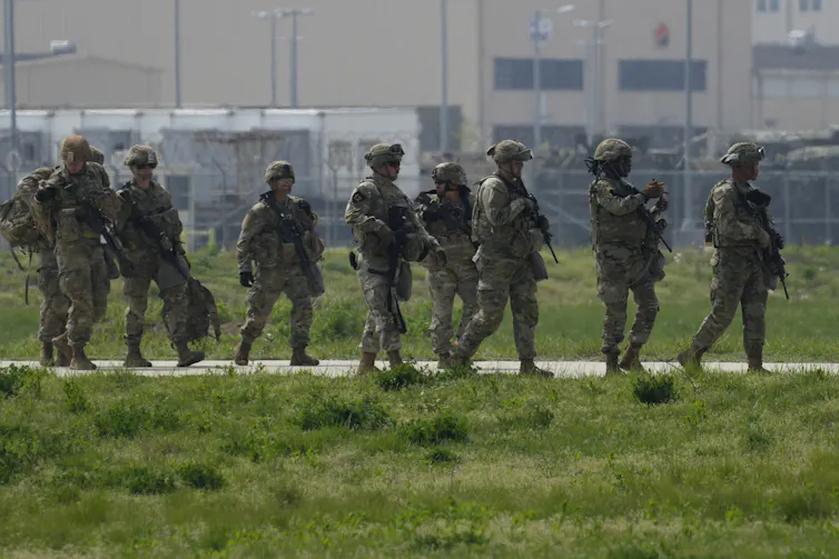 A row of soldiers in battle fatigues walk along a grassy path.