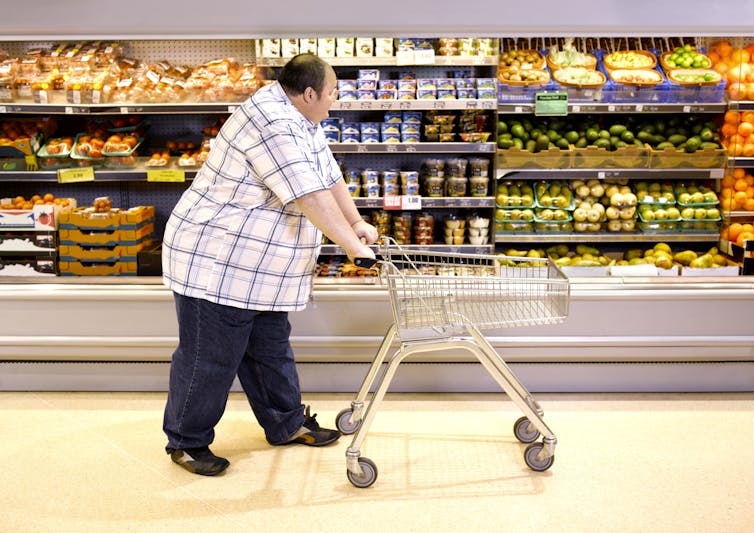 Obese man pushing a cart in a grocery store and peering at healthy food.