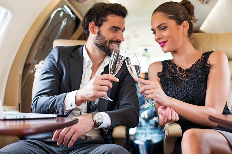a white man and white woman wearing fancy clothes chink champagne glasses in a private jet