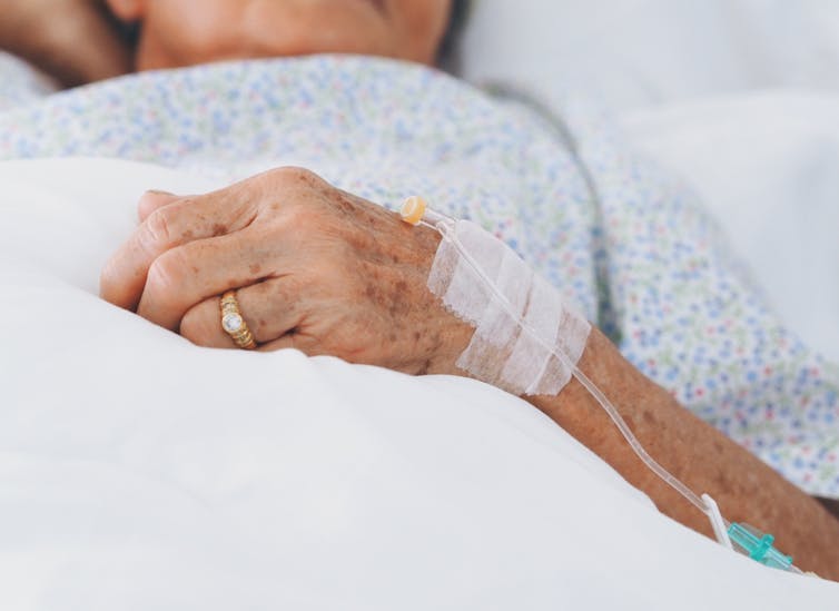 Elderly woman in bed hand on covers