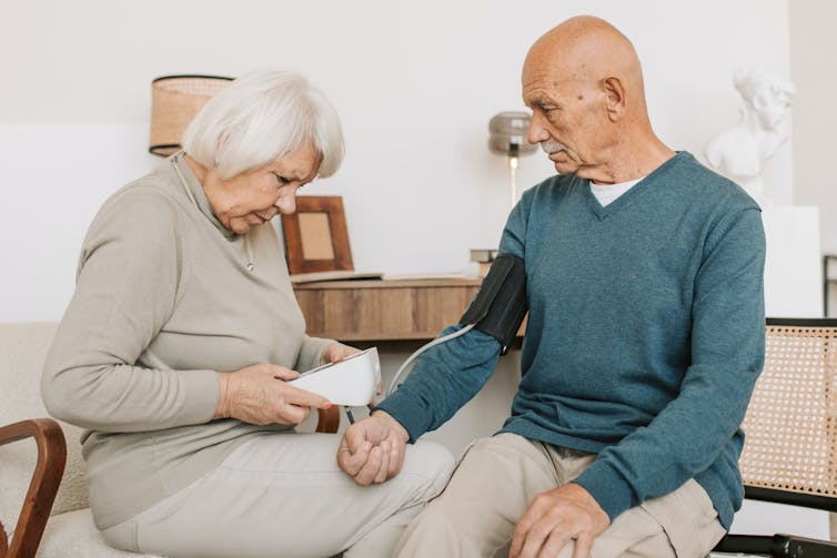 An elderly woman takes an elderly man's blood pressure.