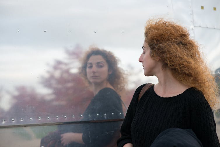 A woman looks at her reflection in a window.