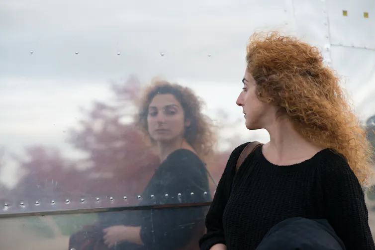 A woman looks at her reflection in a window.