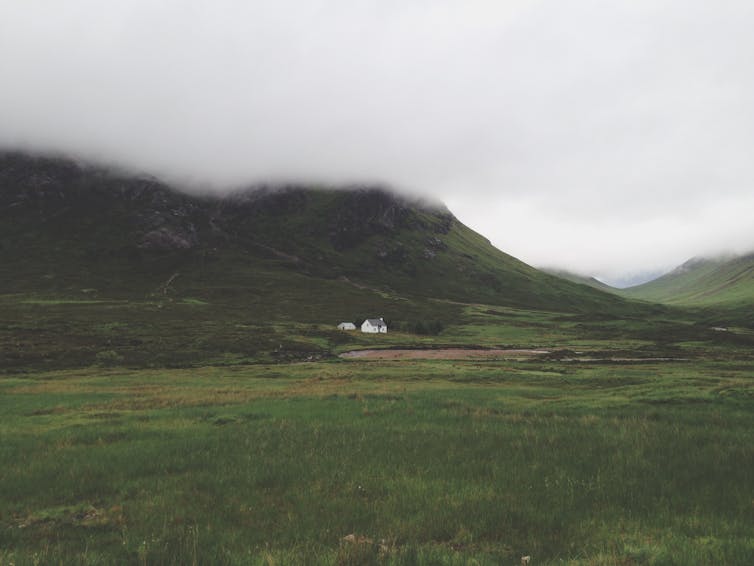 A cottage in a valley with fog overhead.