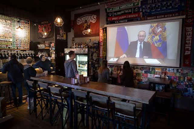 Russian people in the local pub watching Vladimir Putin on TV.