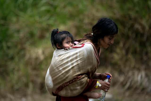 An Ecudaorian migrant carrying her daughter in a sling on her back.
