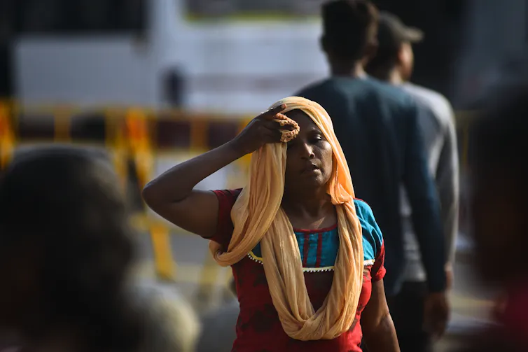 A woman wearing an orange head cloth shades her face from the sun.